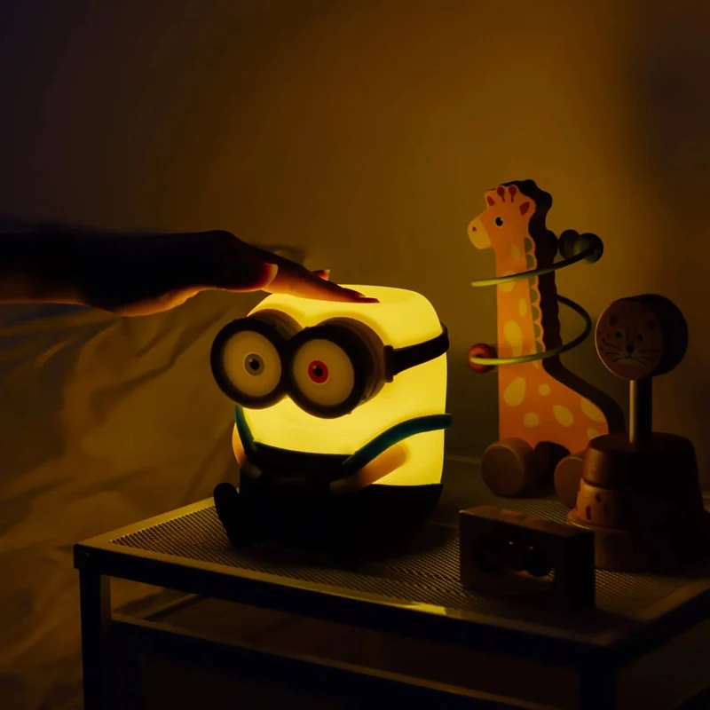 Käsi koskettaa palavan Minions Bob -valaisimen yläosaa sängyn vieressä